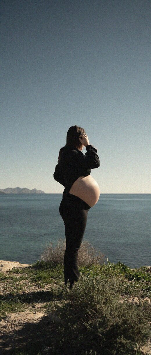 Myriam embarazada, de perfil, mirando al mar desde un acantilado