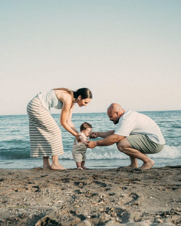 Myriam y su pareja en la orilla de la playa, sujetando de las manos a su bebé